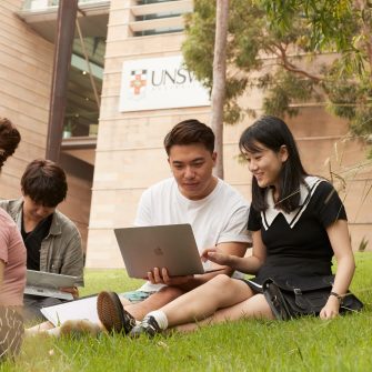 Students with backpacks and laptops sitting outside on campus