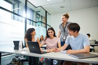 Students in classroom talking to a young staff member