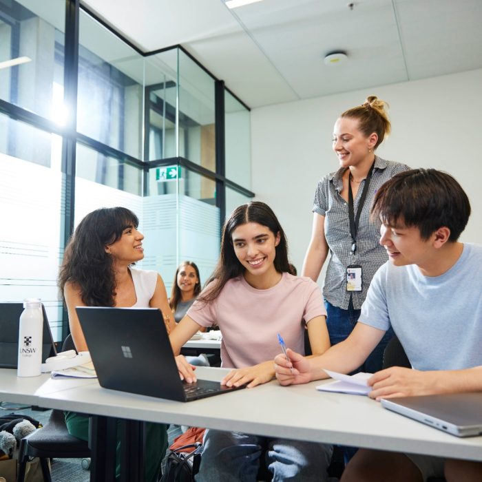 Students in classroom talking to a young staff member