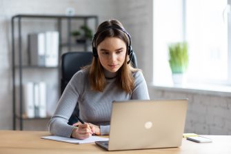 Beautiful young girl studying online using laptop web camera, writing lecture in notebook.Online education, remote working, home education.Online meeting,video call, video conference, courses online.