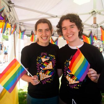 Two people holding rainbow pride flags at a UNSW pride festival stall.