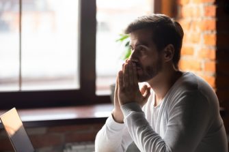 A man holds two hands up to his face looking pensive