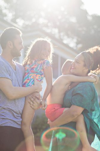 Children sit in a circle around a large piece of fabric painting homes, and rainbows and family