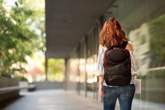 Rear view shot of a young female university student with backpack walking down a paved road