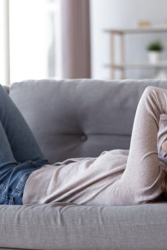 Depressed young person lying on couch at home sufering from fatigue
