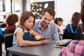 Teacher and young schoolgirl using tablet in classroom