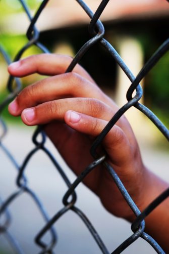 A young person in juvenile detention rests hand  on a mesh fence