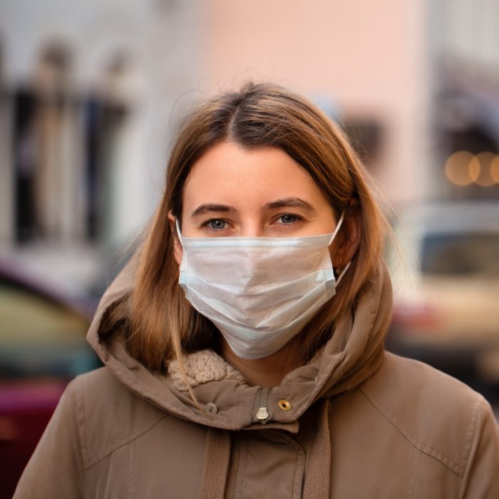 A young woman in a parker wears a surgical mask