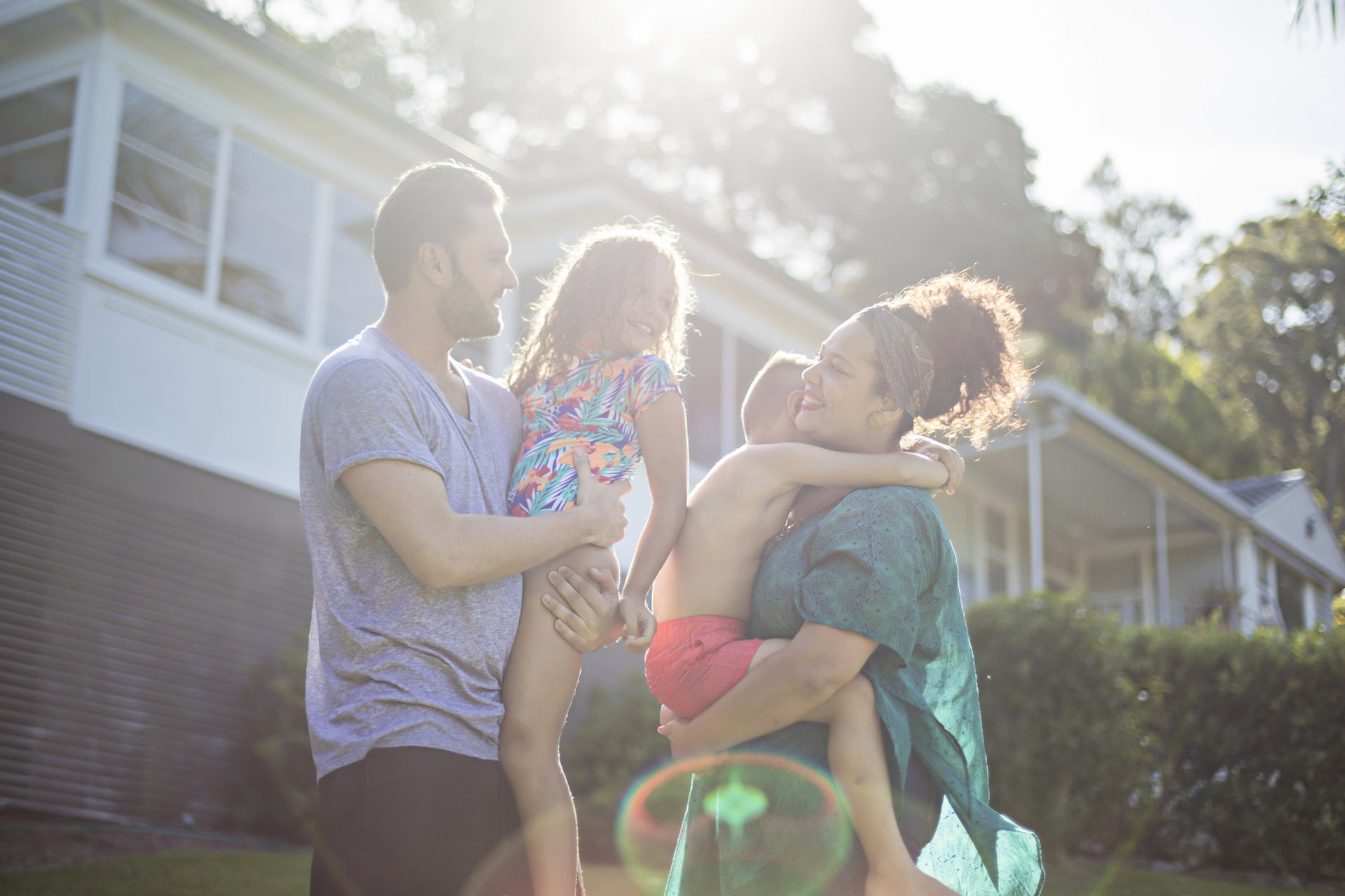 A couple stand holding their young kids in the garden.