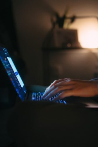 Cropped shot of young Asian woman using laptop at late night in her bedroom. Woman working on laptop typing on keyboard, logging in to her online banking account to manage banking and financial bills. Privacy protection. Working until late at home
