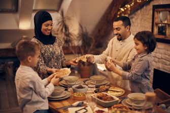 Happy Middle Eastern family shares pita bread at dining table on Ramadan.