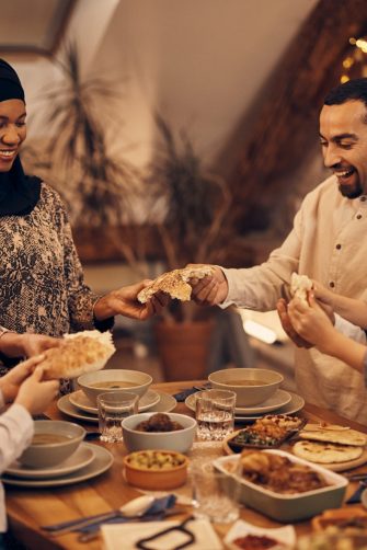 Happy Middle Eastern family shares pita bread at dining table on Ramadan.