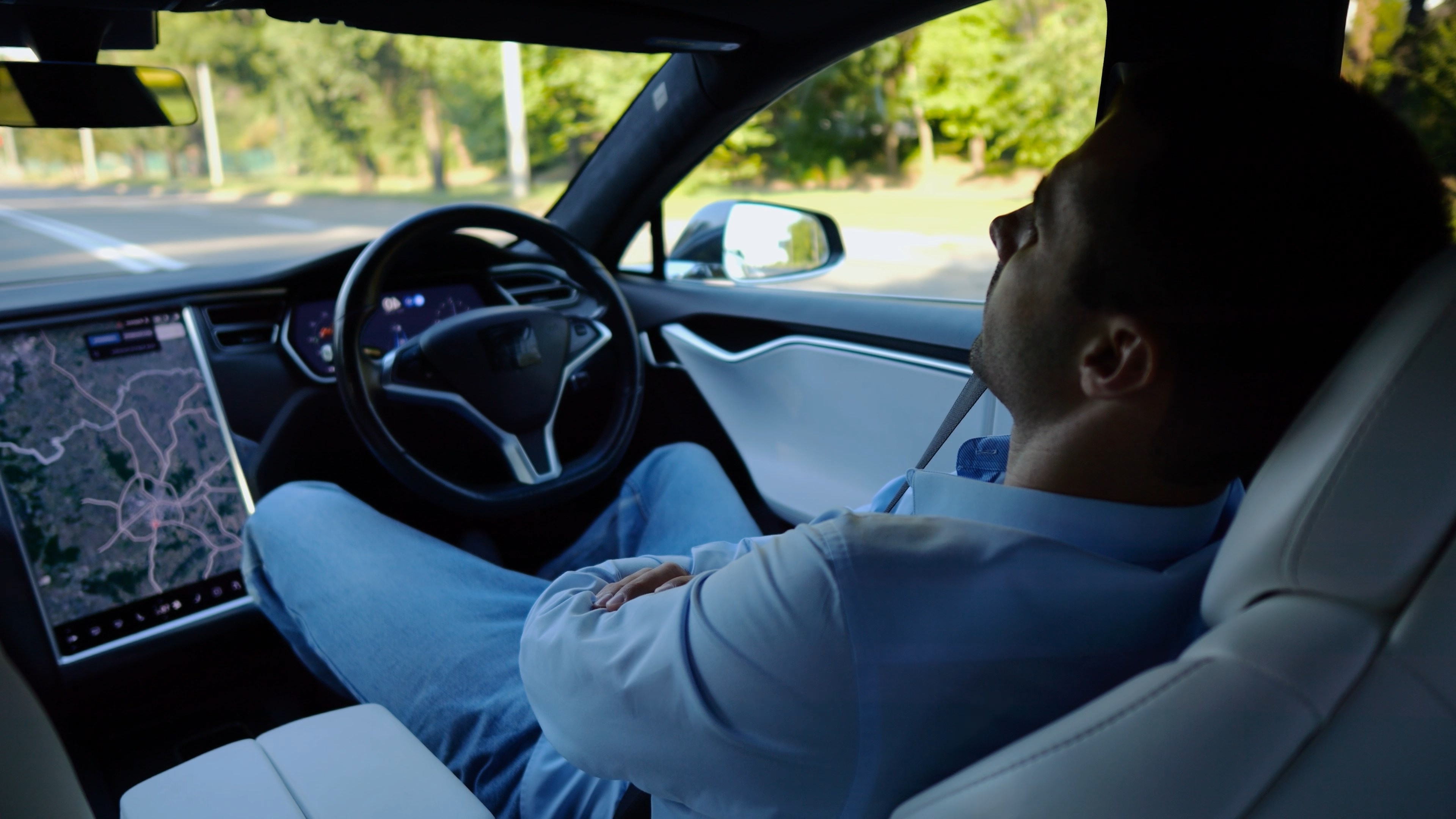 Male businessperson experience to ride an autonomous self driving electric car at urban road. Confident businessman resting during riding on electrical auto with autopilot at city. Slow mo