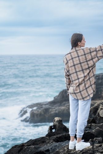 A caucasian person standing on rugged coastal rocks, capturing a selfie with the expansive ocean view in the background. Portugal