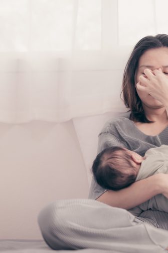 Tired sleepy mother taking care of sick baby at home. Young exhausted woman with toddler at home. Loving mother hugging and comforting crying little son.