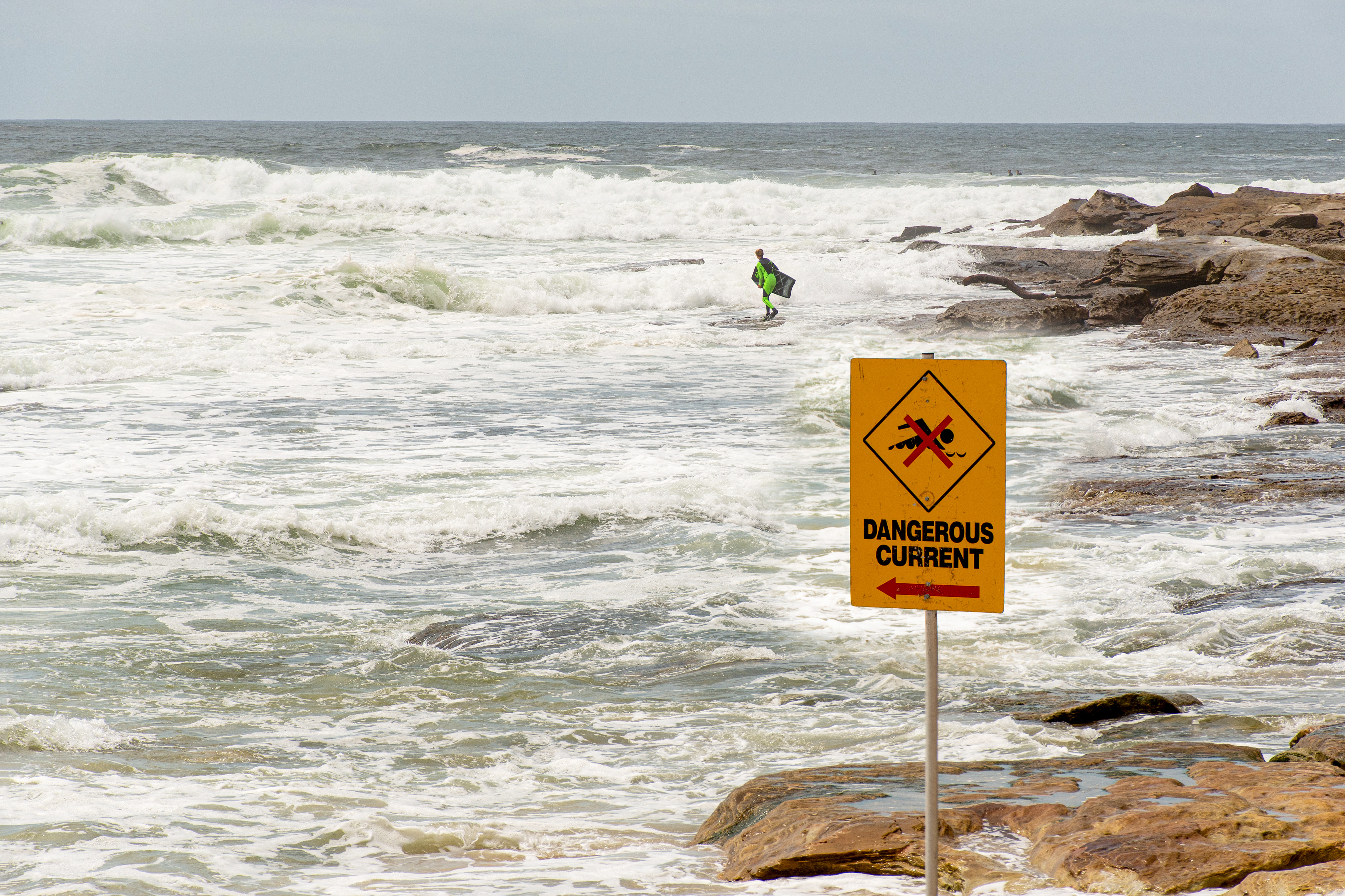 Dangerous current sign for swimmers at the beach in Australia. Lonely surfer entering the water on the background