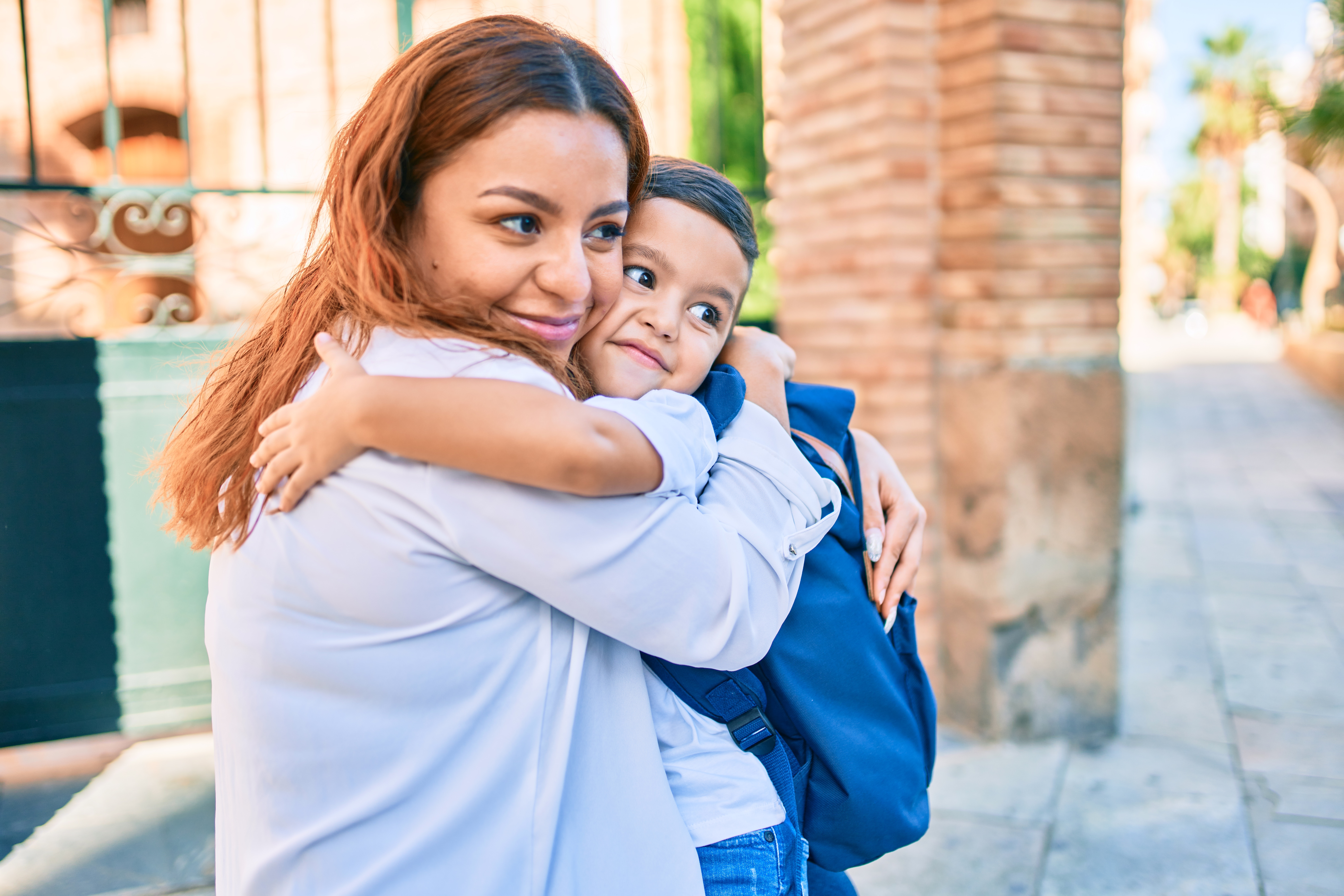 Adorable latin student boy and mom hugging at the city.