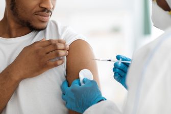 Vaccination and immunization concept. Cropped of young black man receiving vaccine shot during coronavirus pandemic. Closeup of doctor in PPE making injection in shoulder for male patient