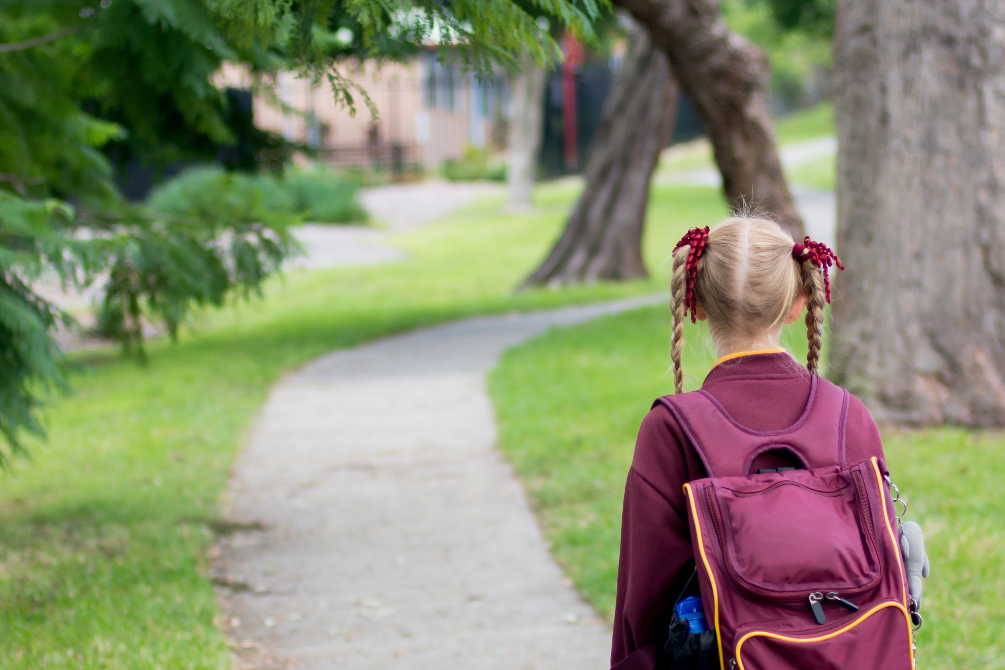 A girl wearing maroon and white school uniform walking to school alone. School students return to classrooms after COVID-19 outbreak in Australia