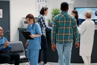 Busy reception desk with many patients waiting to attend consultation, trying to write medical report in hospital lobby. Diverse people having appointments in waiting room area.