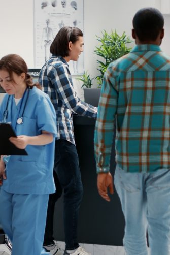 Busy reception desk with many patients waiting to attend consultation, trying to write medical report in hospital lobby. Diverse people having appointments in waiting room area.