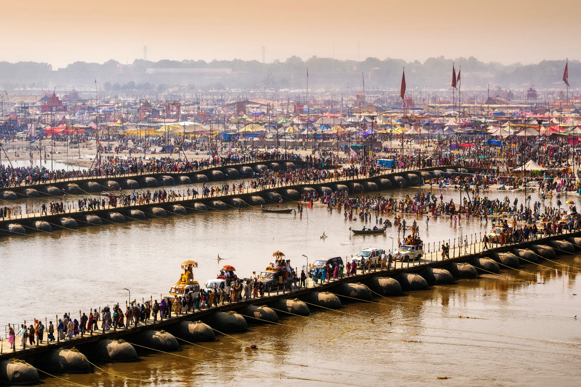 Very large crowds cross pontoon bridges over the Ganges river.
