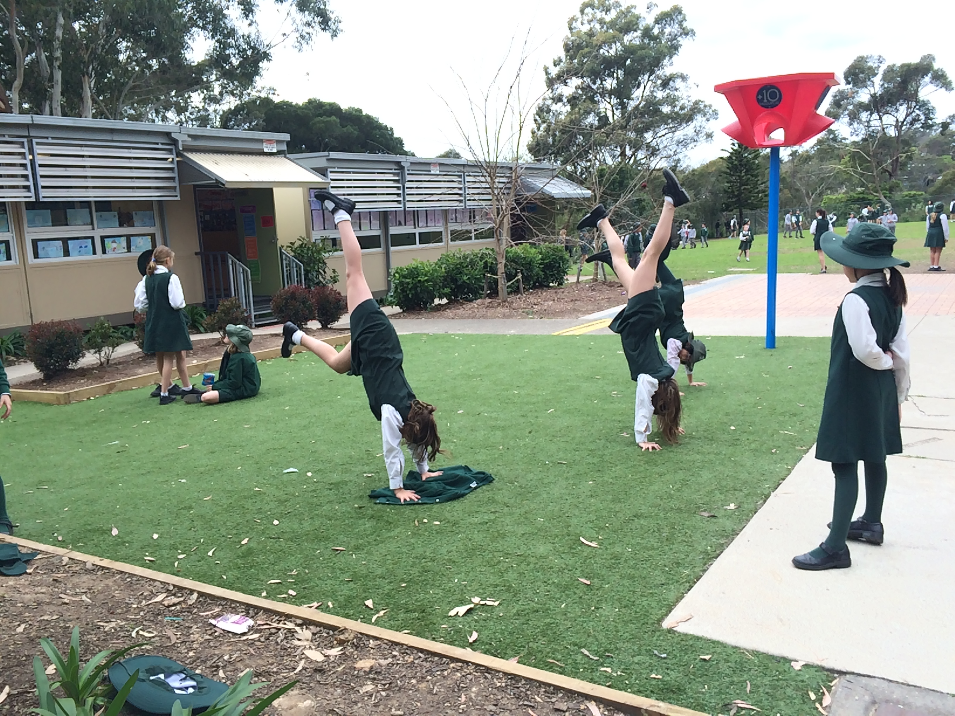 A group of primary school children do handstands on a grassy patch in a school playground