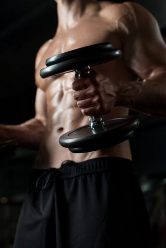 close up of young man with dumbbells flexing muscles in gym