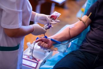 The hand of a man who donates blood. Male donor gives blood in a mobile blood donation center. Blood samples. Hands of the nurse with protective gloves.