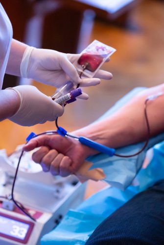 The hand of a man who donates blood. Male donor gives blood in a mobile blood donation center. Blood samples. Hands of the nurse with protective gloves.