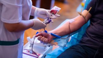 The hand of a man who donates blood. Male donor gives blood in a mobile blood donation center. Blood samples. Hands of the nurse with protective gloves.