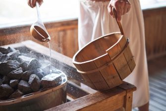 Man pouring water into hot stone in sauna room.