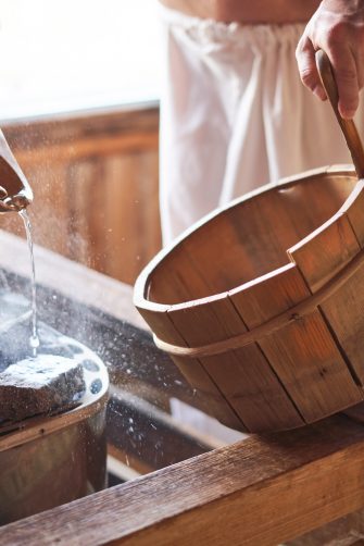 Man pouring water into hot stone in sauna room.