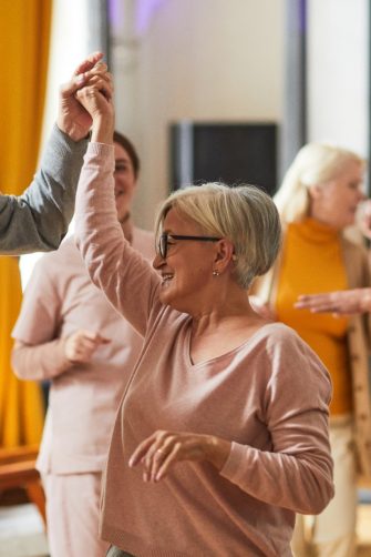 Group of smiling senior people dancing while enjoying activities in retirement home, copy space