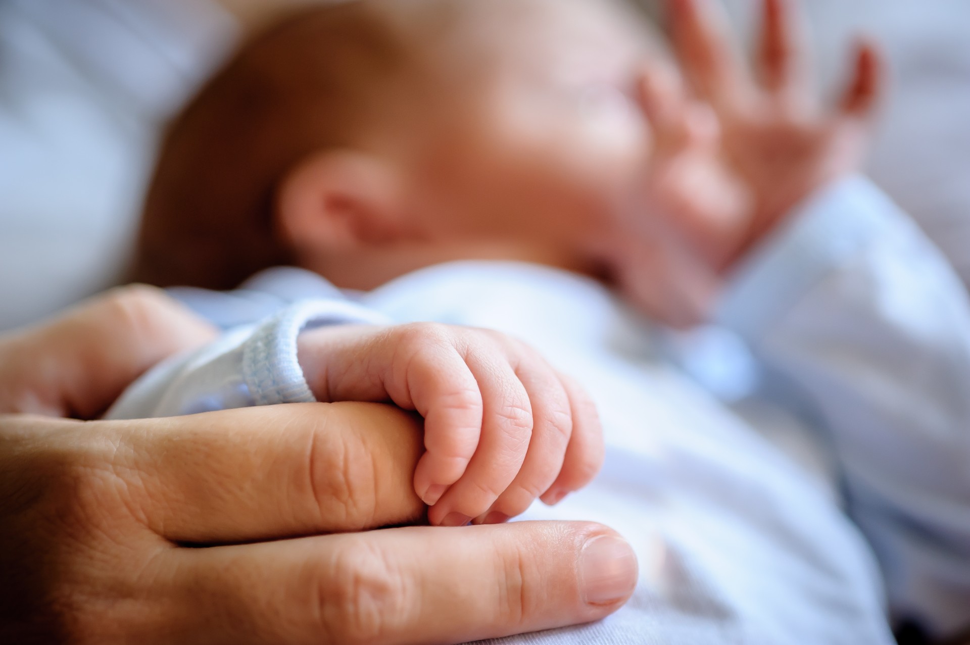 Close-up detail macro view of baby holding on to mom's finger with his little hand. Soft child skin. Love and family emotion