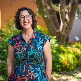 A woman wearing glasses standing and smiling.