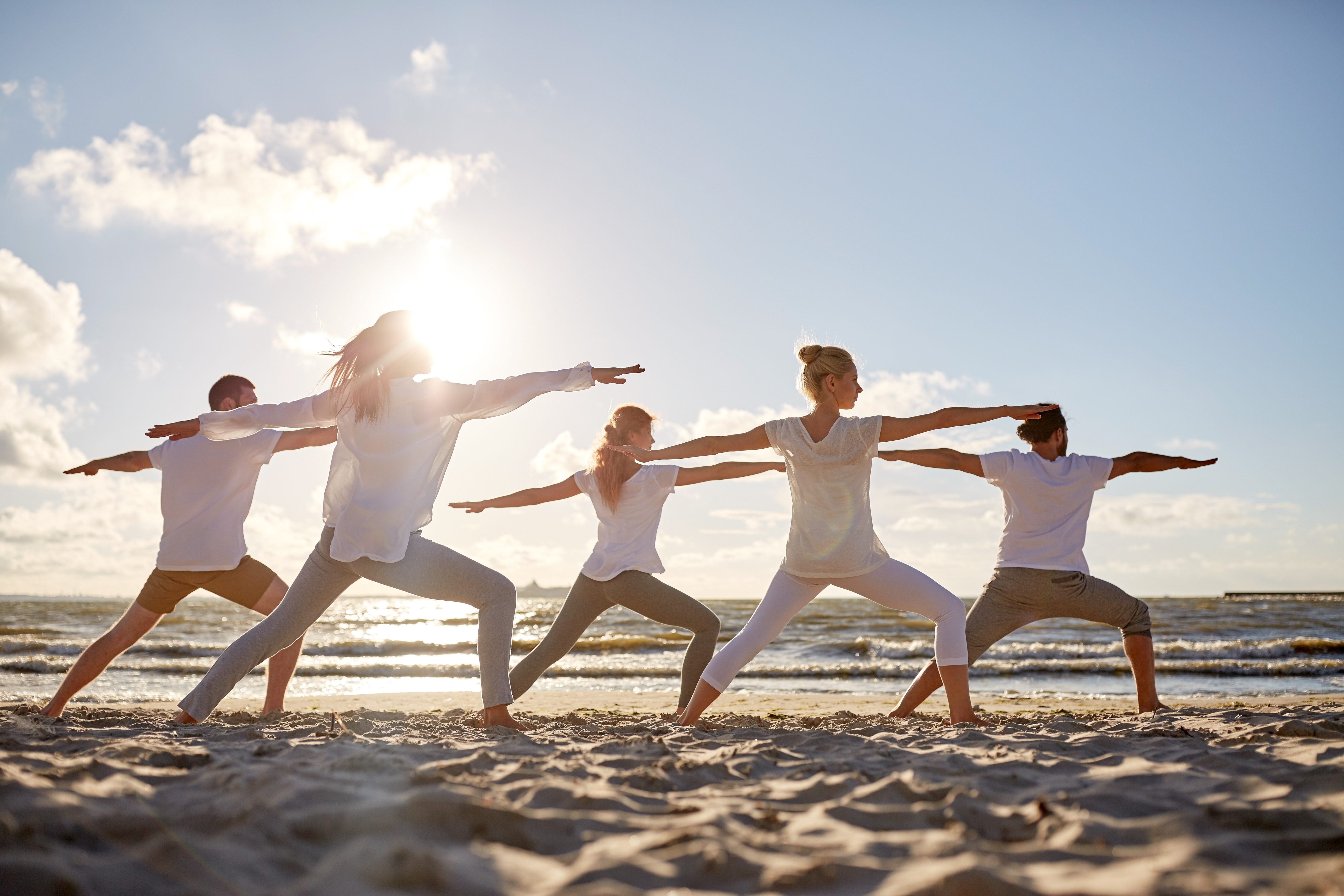 fitness, sport, yoga and healthy lifestyle concept - group of people making warrior pose on beach