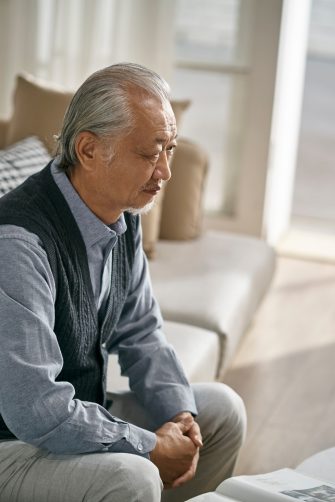 Older Asian man sitting alone at home