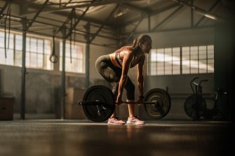 Fit young female athlete lifting heavy weights. Fitness model performing weight lifting exercise at gym.