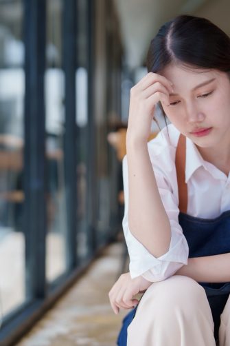 Young woman in apron sitting outside coffee shop feeling overwhelmed and frustrated