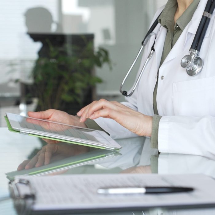 Doctor in white coat with stethoscope using tablet at office desk, reviewing digital patient data for telehealth and clinical care innovations. Medicine and health care concept