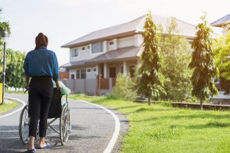 young woman or social worker assisting or strolling with patient or elderly disabled on wheelchair in city park. Wheelchair disabled. Helping elderly disabled man relaxing or exercise at house
