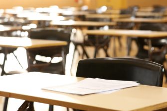 A large high school hall or room set up ready for an end of year final exam to be sat by students. examination paper sitting on the edge of a desk or table. 