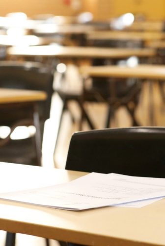 A large high school hall or room set up ready for an end of year final exam to be sat by students. examination paper sitting on the edge of a desk or table. 