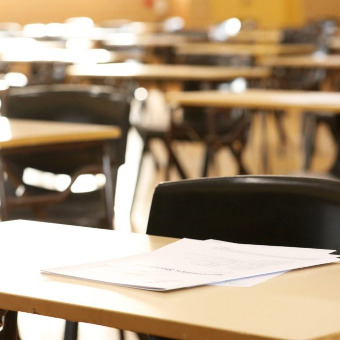 A large high school hall or room set up ready for an end of year final exam to be sat by students. examination paper sitting on the edge of a desk or table. 