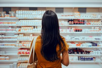 Young woman standing against shelf in pharmacy searching for medicine