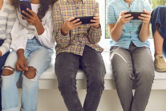 Cropped shot of children immersed in mobile devices. Kids sitting on windowsill and ignoring real life playing online games, chatting on social media, blogging or checking newsfeed using cell phones