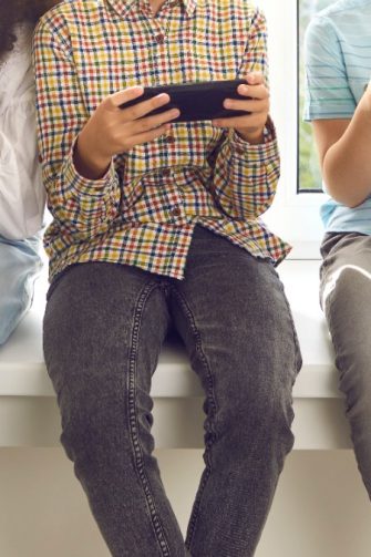 Cropped shot of children immersed in mobile devices. Kids sitting on windowsill and ignoring real life playing online games, chatting on social media, blogging or checking newsfeed using cell phones