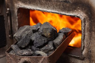 Solid fuel boiler with opened door and fire inside, scoop with coal nearby. Alternative ways of heating the house in cold winter season