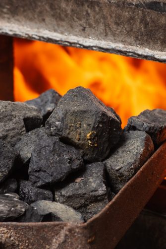 Solid fuel boiler with opened door and fire inside, scoop with coal nearby. Alternative ways of heating the house in cold winter season